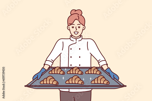 Woman baker holds tray of croissants preparing fresh pastries for sale in own bakery. Girl cook and owner of bakery with smile demonstrates delicious sweet buns for breakfast or lunch