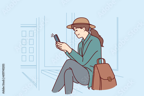 Woman is sitting at bus stop using phone to track public transport via GPS navigation. Successful girl tourist waiting for bus or tram after arriving in new city for business trip.