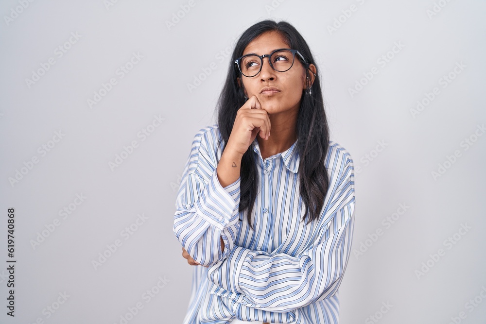Young hispanic woman wearing glasses with hand on chin thinking about question, pensive expression. smiling with thoughtful face. doubt concept. Young hispanic woman wearing glasses with hand on chin thinking about question, pensive expression. smiling with thoughtful face. doubt concept.