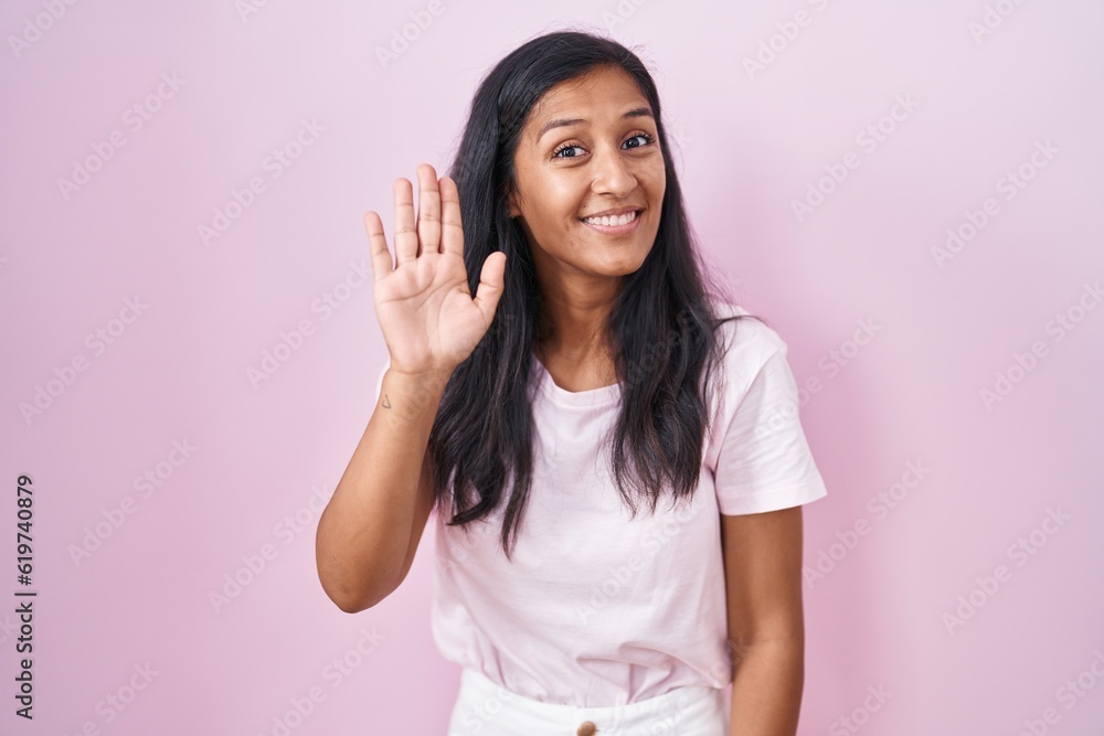 Young hispanic woman standing over pink background waiving saying hello happy and smiling, friendly welcome gesture Young hispanic woman standing over pink background waiving saying hello happy and smiling, friendly welcome gesture