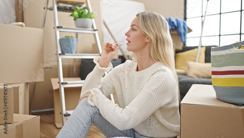 Young blonde woman sitting on floor with doubt expression at new home