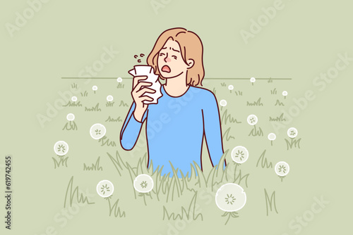Woman sneezes because of allergy caused by dandelion blossoms and pollen from summer plants. Unhappy girl with handkerchief needs allergy medicine to stop irritation of mucous membranes of nose.