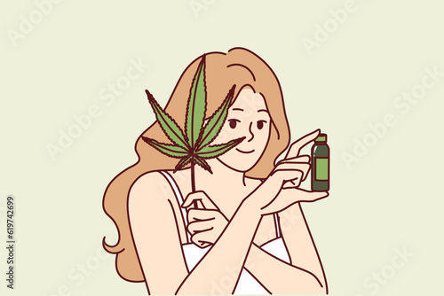 Woman uses hemp oil for skin care and fighting acne or wrinkles on face and holds marijuana leaf in hand. Girl recommends hemp cosmetic product for anti-aging, concept of weed for medical purposes