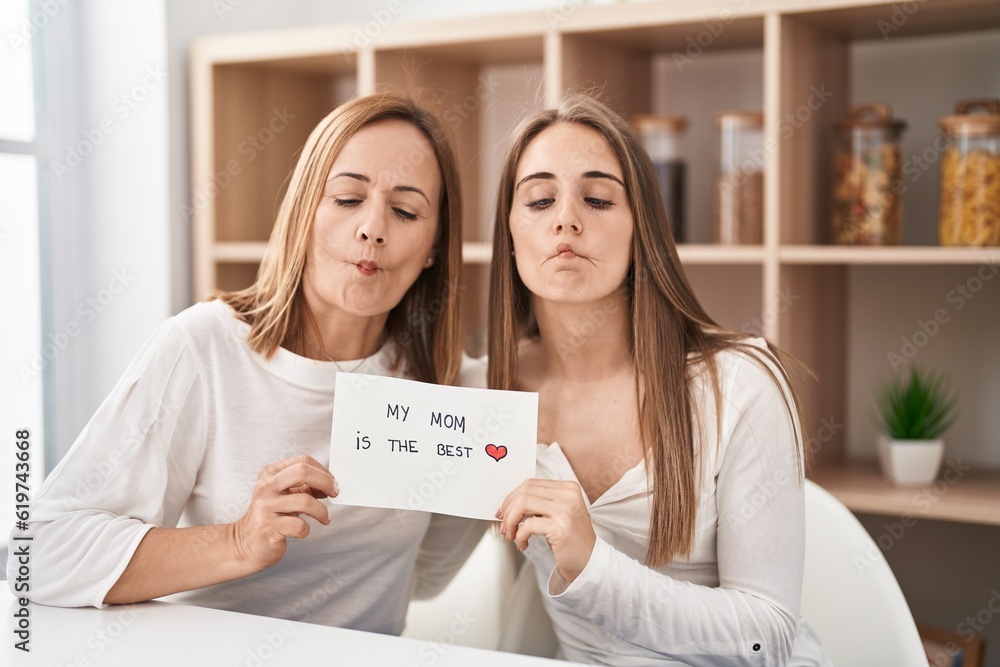 Middle age mother and young daughter holding my mom is the best banner making fish face with mouth and squinting eyes, crazy and comical. Middle age mother and young daughter holding my mom is the best banner making fish face with mouth and squinting eyes, crazy and comical.