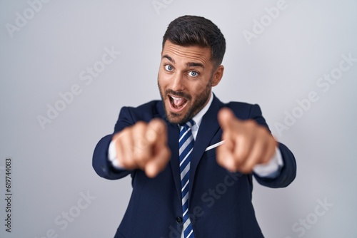 Handsome hispanic man wearing suit and tie pointing to you and the camera with fingers, smiling positive and cheerful