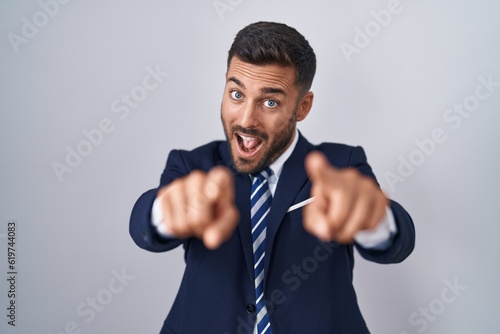 Handsome hispanic man wearing suit and tie pointing to you and the camera with fingers, smiling positive and cheerful photo