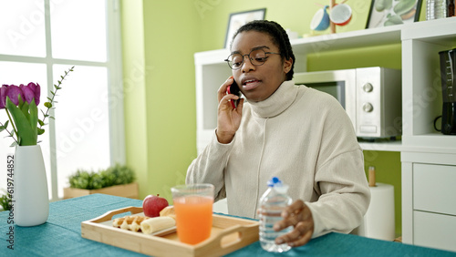 African american woman having breakfast talking on smartphone at dinning room
