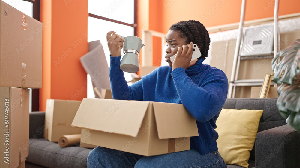 African american woman speaking on the phone unpacking cardboard box at new home African american woman speaking on the phone unpacking cardboard box at new home