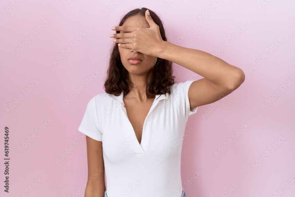 Young hispanic woman wearing casual white t shirt covering eyes with hand, looking serious and sad. sightless, hiding and rejection concept Young hispanic woman wearing casual white t shirt covering eyes with hand, looking serious and sad. sightless, hiding and rejection concept