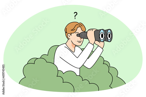 Man looking in binoculars from bush