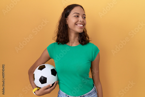 Young hispanic woman holding ball looking away to side with smile on face, natural expression. laughing confident. © Krakenimages.com
