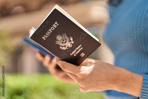 Young african american woman holding united states passport using smartphone at park