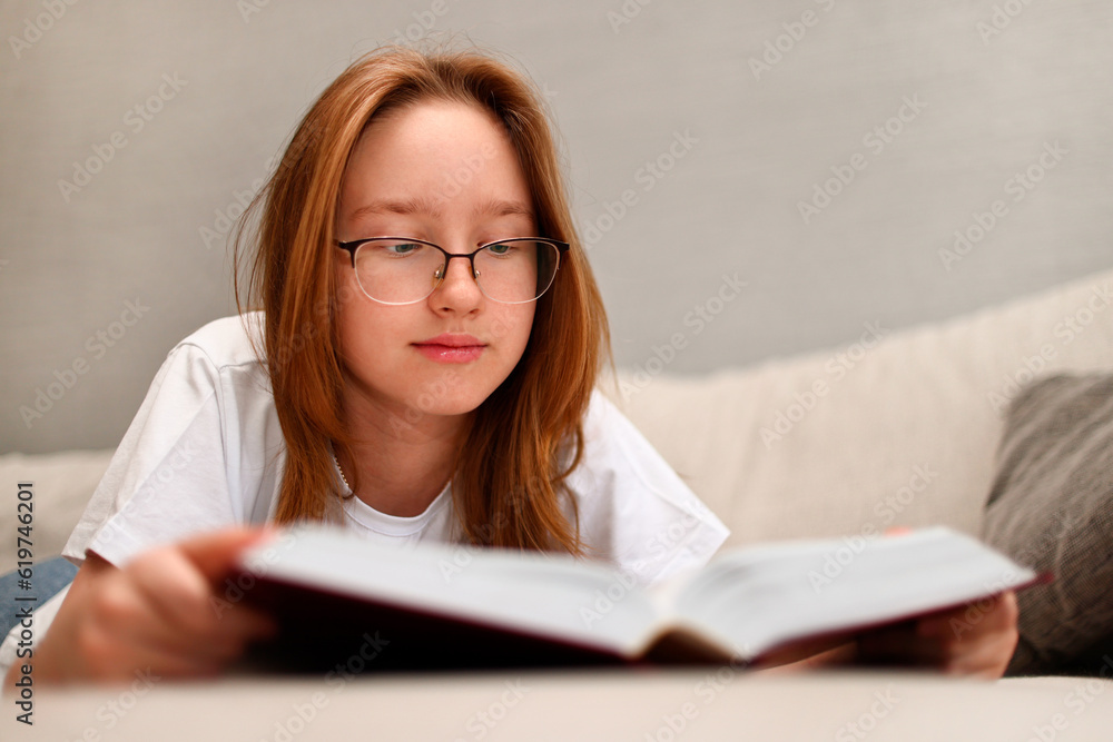 The girl is reading a thick book lying on the sofa. The girl is reading a thick book lying on the sofa.