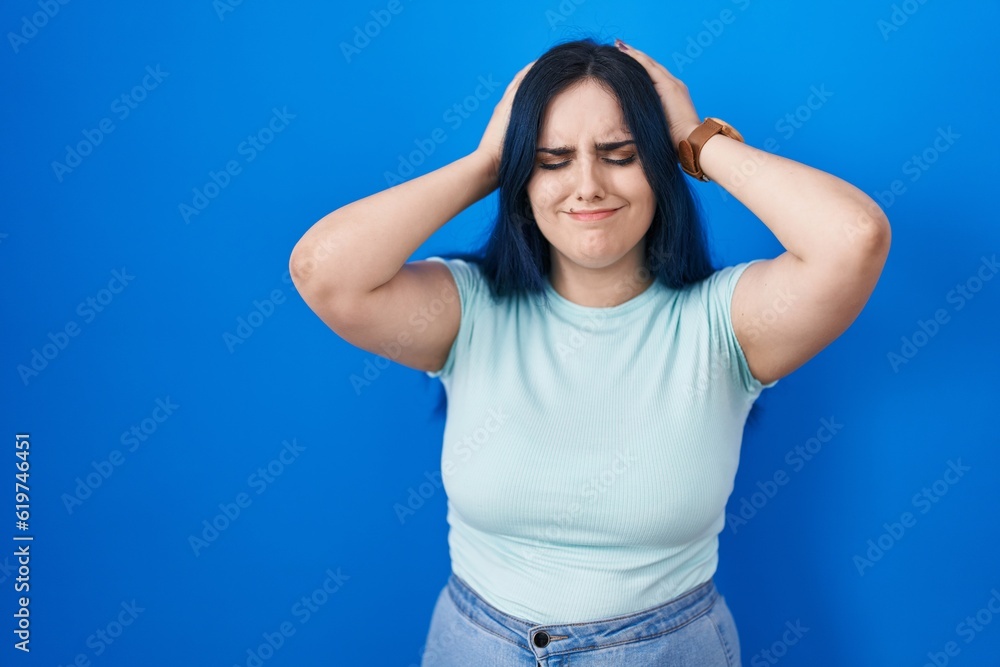 Young modern girl with blue hair standing over blue background suffering from headache desperate and stressed because pain and migraine. hands on head. Young modern girl with blue hair standing over blue background suffering from headache desperate and stressed because pain and migraine. hands on head.