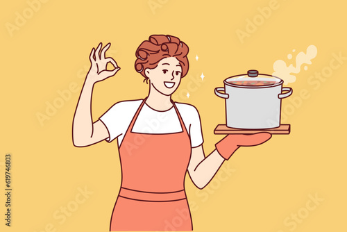 Woman housewife or cook with soup pan shows ok gesture and looks at screen smiling. Happy girl housewife in apron invites to have lunch and eat homemade food from healthy ingredients