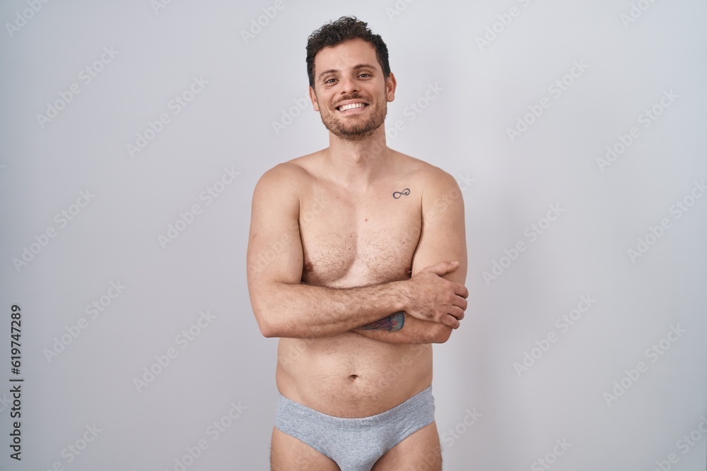 Young hispanic man standing shirtless wearing underware happy face smiling with crossed arms looking at the camera. positive person.
