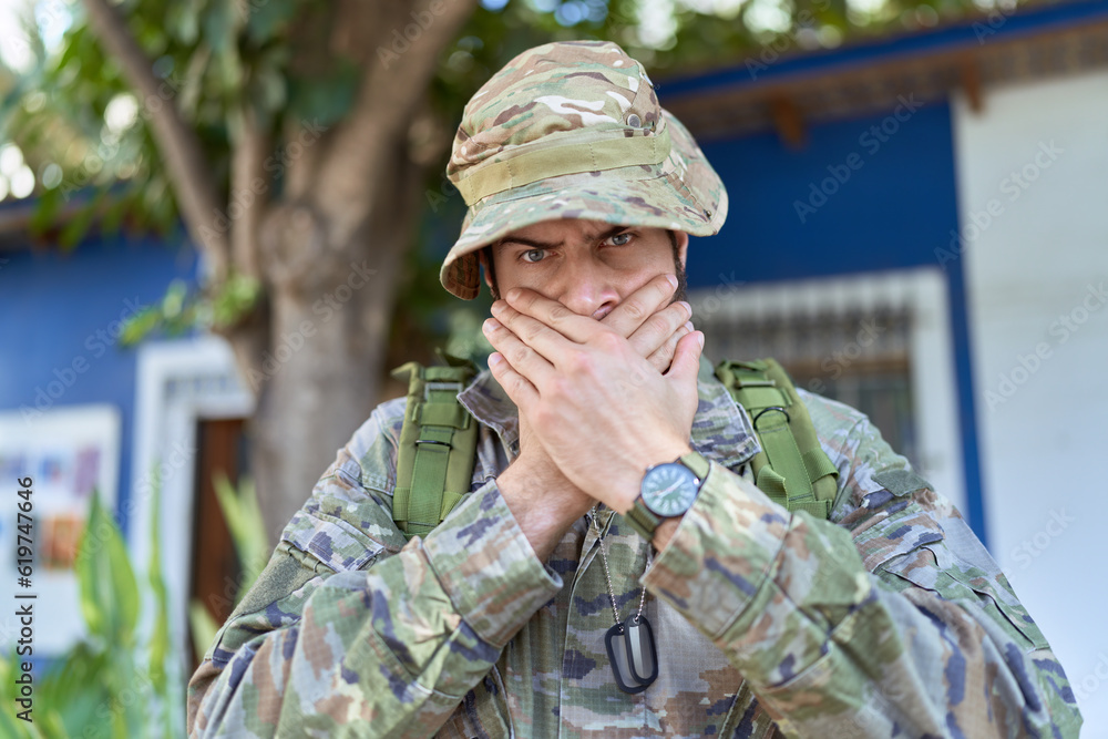 Young hispanic man wearing camouflage army uniform outdoors shocked covering mouth with hands for mistake. secret concept.