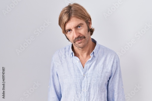 Caucasian man with mustache standing over white background looking sleepy and tired, exhausted for fatigue and hangover, lazy eyes in the morning.