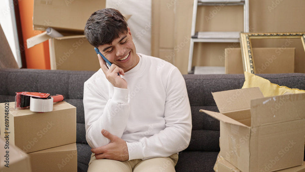 Young hispanic man talking on smartphone sitting on sofa at new home Young hispanic man talking on smartphone sitting on sofa at new home