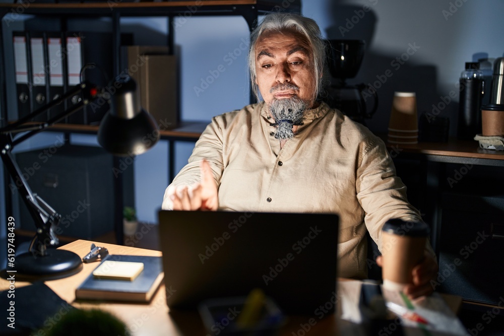 Middle age man with grey hair working at the office at night pointing with finger up and angry expression, showing no gesture Middle age man with grey hair working at the office at night pointing with finger up and angry expression, showing no gesture