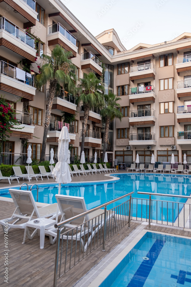 Luxurious hotel with swimming pool, palm trees, sun loungers and seating area. Palm trees are reflected in the clear water of the pool.