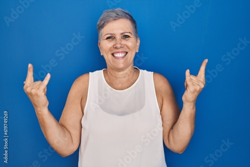 Middle age caucasian woman standing over blue background shouting with crazy expression doing rock symbol with hands up. music star. heavy concept. © Krakenimages.com