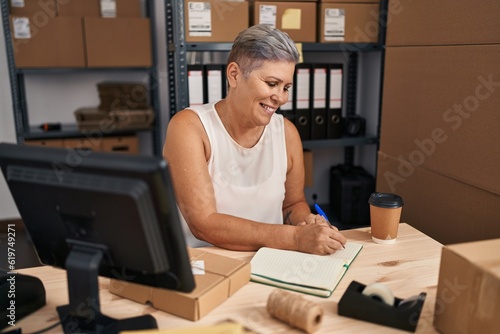Middle age woman ecommerce business worker writing on book at office