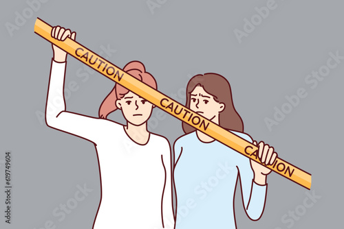 Women near yellow caution tape prohibiting passage to crime scene or territory closed to strangers. Two girls are unhappy with restriction and caution tape restricting freedom of movement