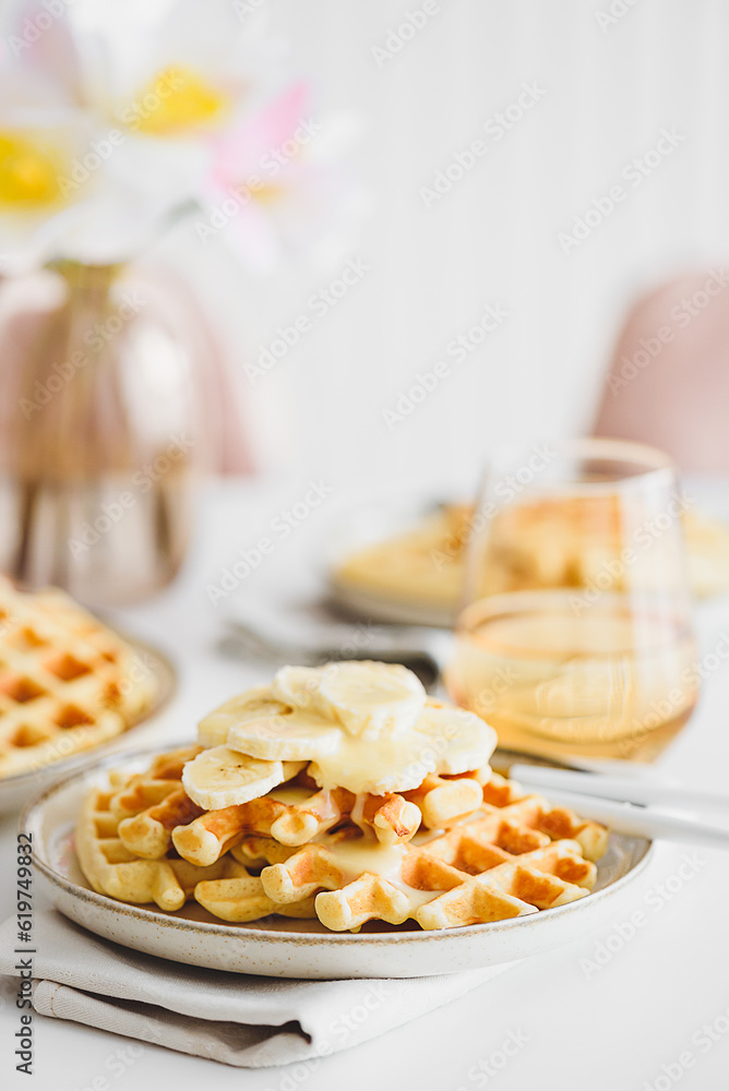 Belgian waffles with banana and condensed milk on white table