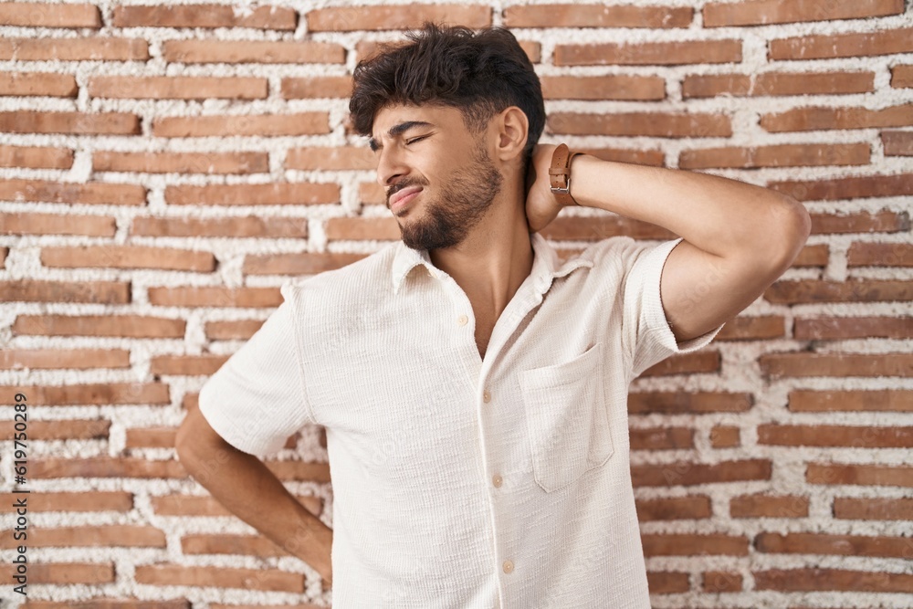 Arab man with beard standing over bricks wall background suffering of neck ache injury, touching neck with hand, muscular pain Arab man with beard standing over bricks wall background suffering of neck ache injury, touching neck with hand, muscular pain
