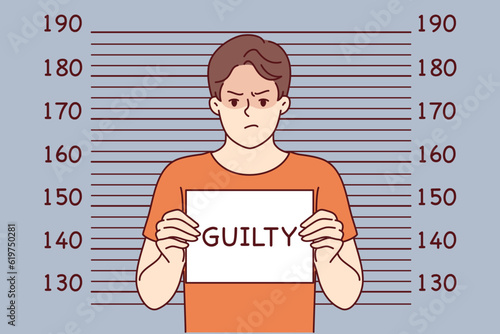 Man criminal with inscription guilty on sign stands near lines for measuring height of arrested bandit. Guilty guy who committed crime is detained by police and needs help of lawyer for court hearing