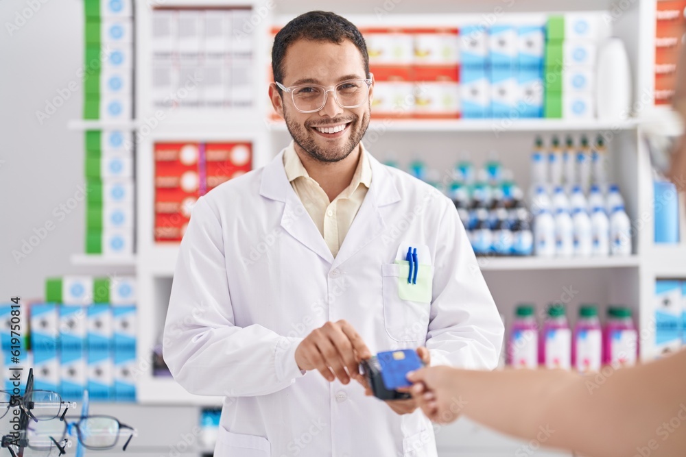 Young man pharmacist using credit card and dataphone at pharmacy