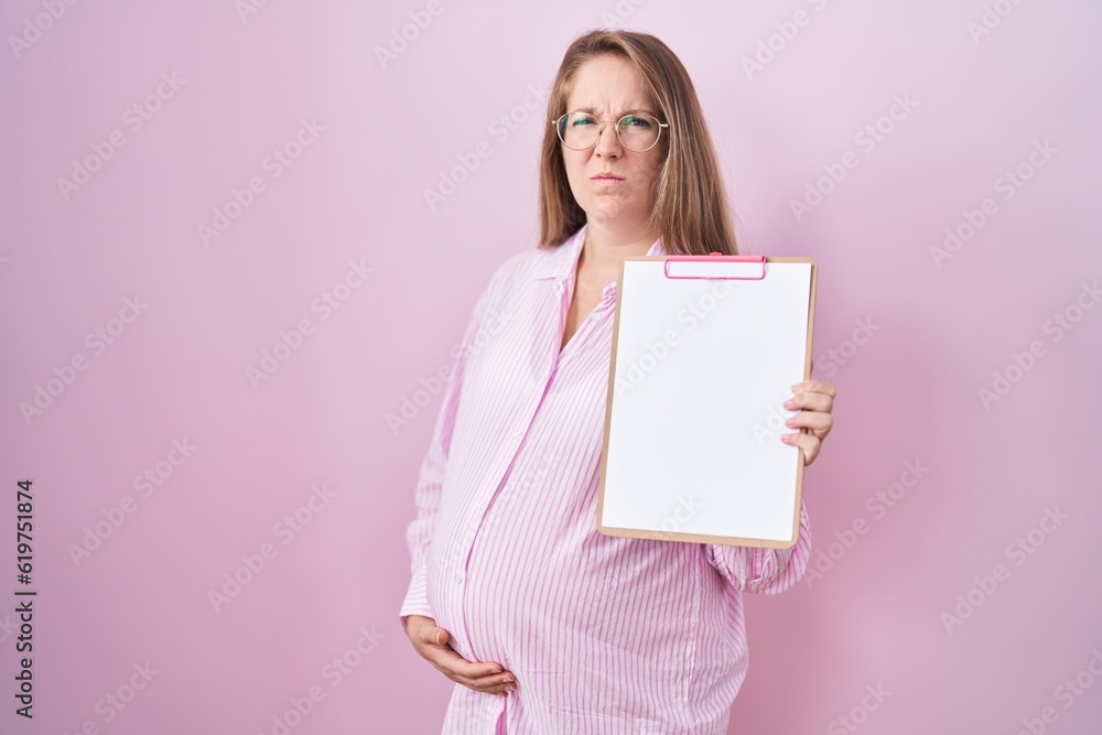 Young pregnant woman holding clipboard skeptic and nervous, frowning upset because of problem. negative person. Young pregnant woman holding clipboard skeptic and nervous, frowning upset because of problem. negative person.