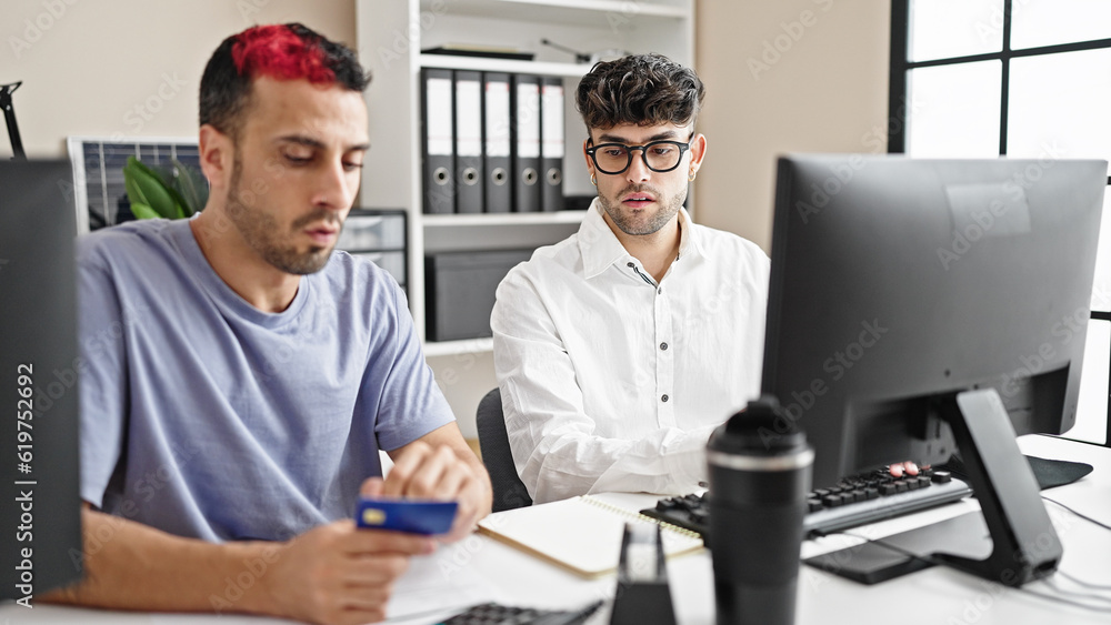 Two men business workers using computer and credit card at office Two men business workers using computer and credit card at office