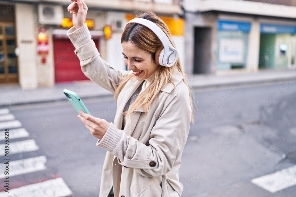 Fototapeta premium Young blonde woman listening to music and dancing at street