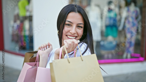 Young beautiful hispanic woman smiling going shopping holding bags at clothing store