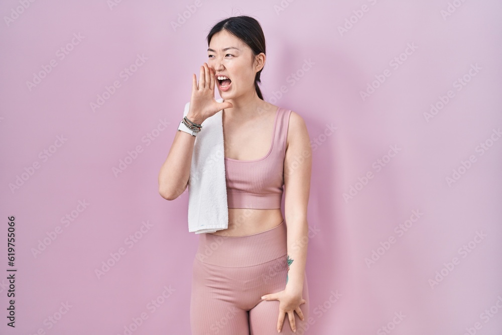 Chinese young woman wearing sportswear and towel shouting and screaming loud to side with hand on mouth. communication concept. Chinese young woman wearing sportswear and towel shouting and screaming loud to side with hand on mouth. communication concept.
