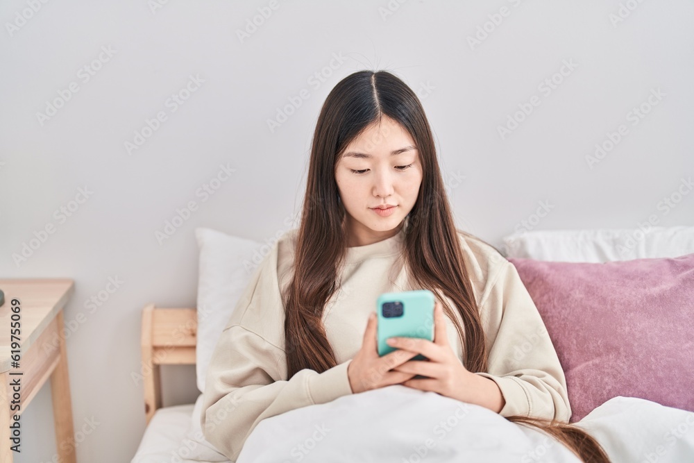 Chinese woman using smartphone sitting on bed at bedroom Chinese woman using smartphone sitting on bed at bedroom