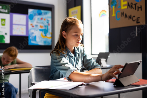 Caucasian schoolgirl sitting at desk and using tablet in school classroom