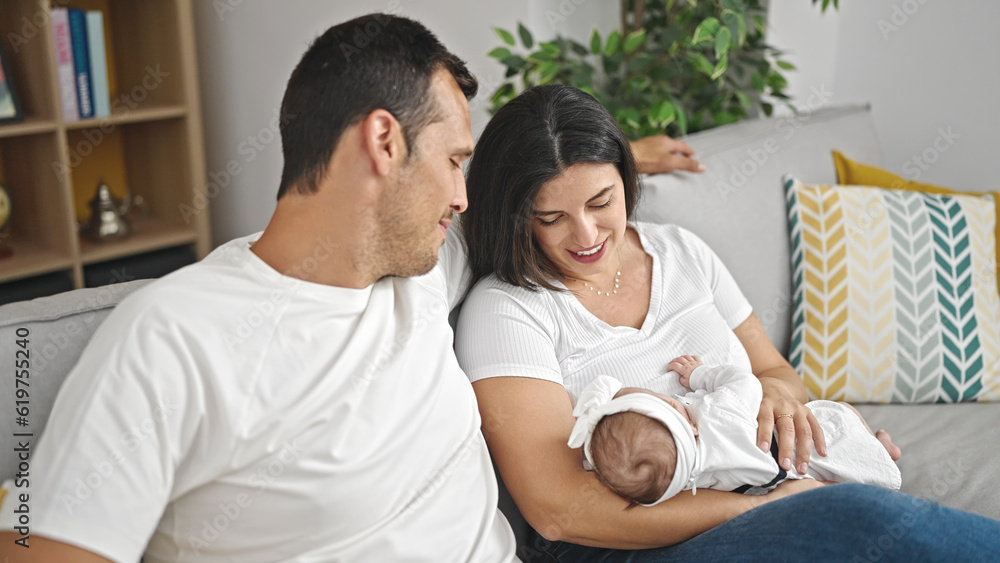 Family of three bonding and breastfeeding sitting on the sofa at home Family of three bonding and breastfeeding sitting on the sofa at home