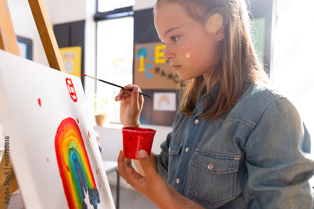 Naklejka premium Caucasian schoolgirl painting using brush and easel in school art class