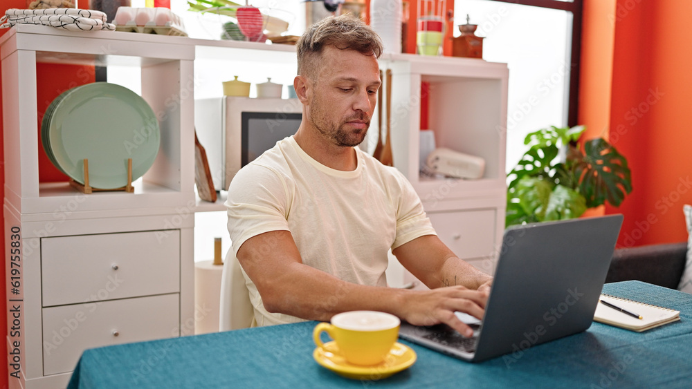 Young man drinking coffee using laptop sitting on table at dinning room Young man drinking coffee using laptop sitting on table at dinning room