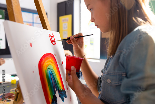 Caucasian schoolgirl having art class and painting rainbow in classroom