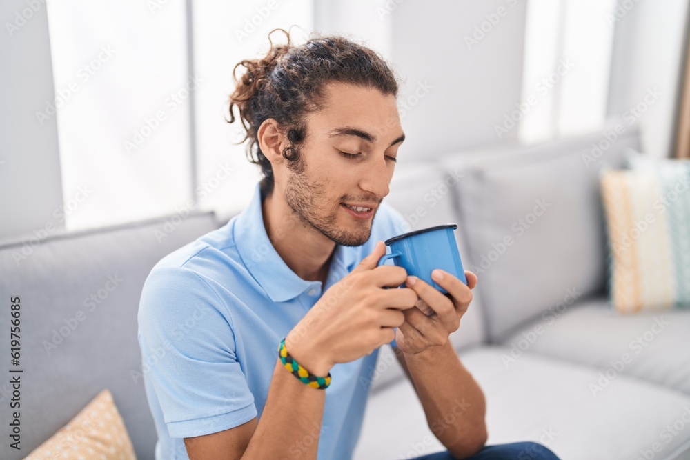 Young hispanic man drinking coffee sitting on sofa at home Young hispanic man drinking coffee sitting on sofa at home