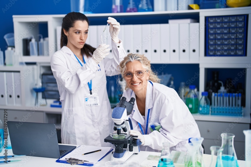 Two women scientists using microscope measuring liquid at laboratory