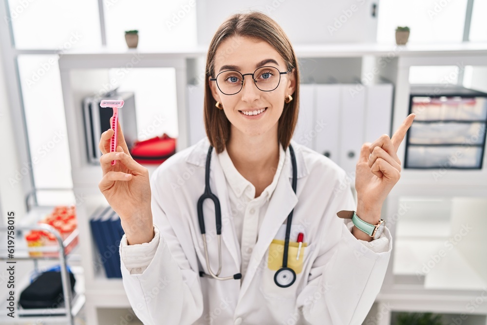 Young caucasian doctor woman holding razor smiling happy pointing with hand and finger to the side Young caucasian doctor woman holding razor smiling happy pointing with hand and finger to the side