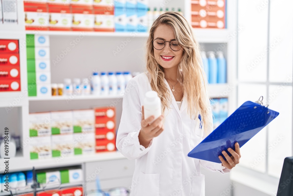 Young woman pharmacist reading report holding pills bottle at pharmacy