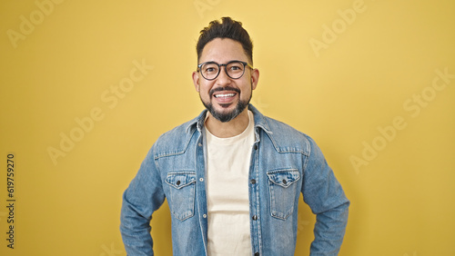Young latin man smiling confident standing over isolated yellow background