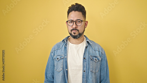 Young latin man standing with serious expression over isolated yellow background © Krakenimages.com