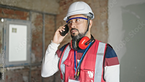 Young latin man builder talking on walkie-talkie at construction site